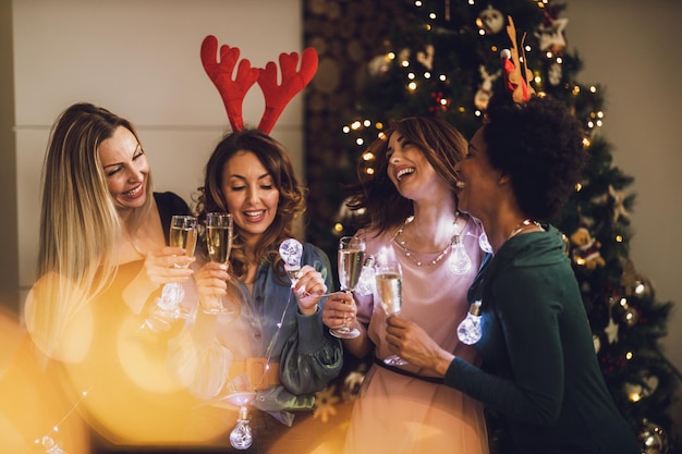 Alegres amigas multiétnicas divirtiéndose mientras brindan con champán en Navidad o en la fiesta de Año Nuevo juntas.