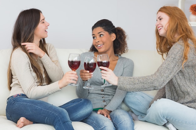 Alegres amigas tostando copas de vino en casa