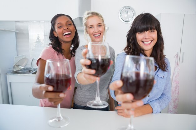 Alegres amigos brindando a la cámara con vasos de vino tinto