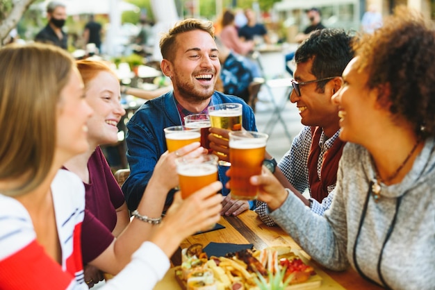 Alegres amigos multiétnicos tintineando vasos de cerveza