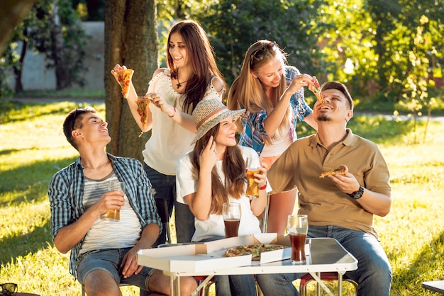 Alegres amigos de picnic en el parque. Comiendo pizza