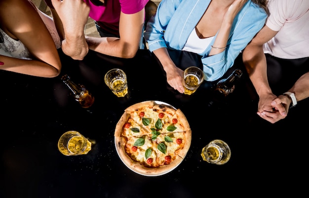 Alegres amigos en el pub. Beber cerveza, comer pizza, hablar, divertirse.