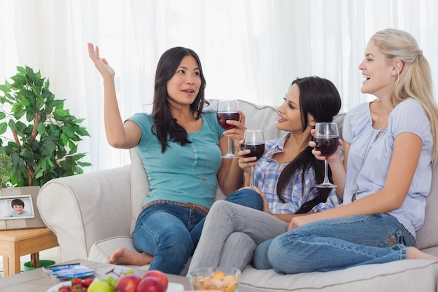 Alegres amigos tomando vinho tinto juntos e conversando em casa no sofá