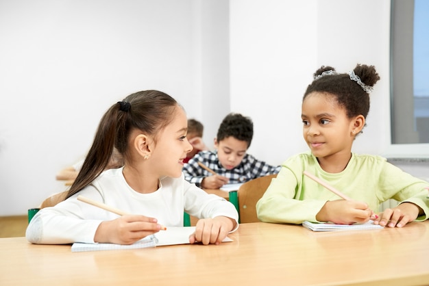 Alegres compañeros sentados a la mesa en el aula en la escuela