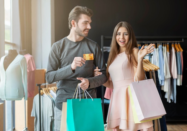 Alegres compradores caucásicos con bolsas de compras y tarjeta de crédito, fondo de sala de exposición