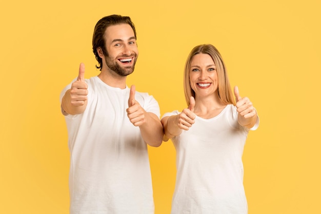 Alegres e felizes homens e mulheres caucasianos do milênio em camisetas brancas mostram os polegares para cima aprovando a oferta