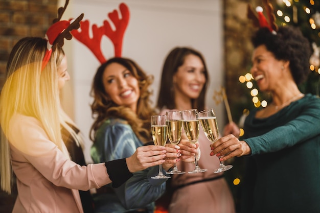 Alegres garotas multiétnicas brindando com champanhe na festa de Natal ou ano novo. Close-up nas taças de vinho.