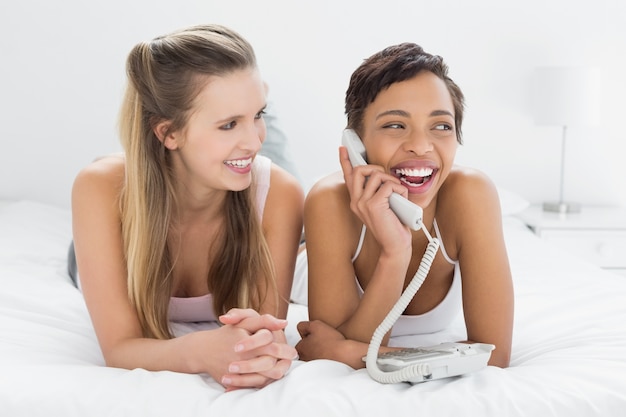 Alegres jóvenes amigas usando el teléfono en la cama