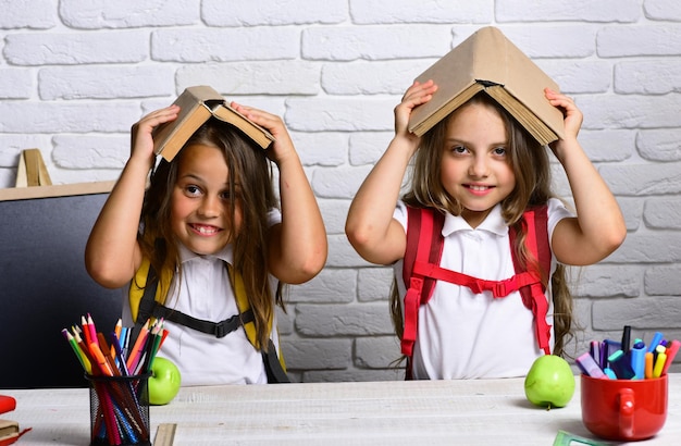 Alegres meninas sorridentes com livros na cabeça. Olhando para a câmera. Conceito de escola. De volta à escola.