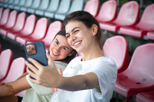 Alegres mujeres jóvenes atléticas tomando selfie por teléfono inteligente en la tribuna