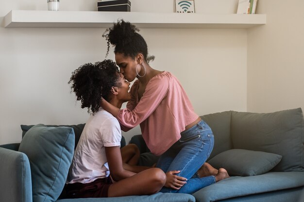 Alegres namoradas jovens abraçando e beijando no sofá em casa