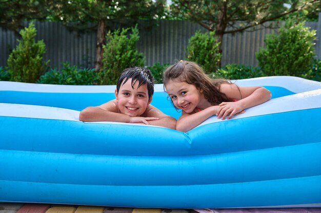 Alegres niños caucásicos hermanos y hermanas nadan en la piscina inflable y sonríen lindamente mirando la cámara