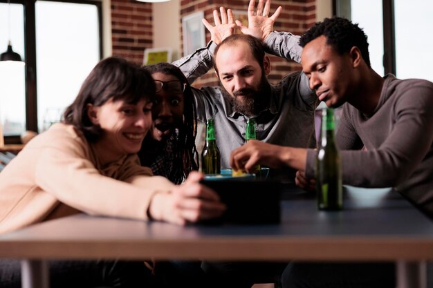 Alegres pessoas diversas com dispositivo smartphone moderno tirando foto de grupo selfie juntos. Jovens adultos positivos sentados em casa na sala de estar com celular enquanto tiram foto.