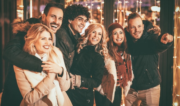 Alegres seis amigos sorridentes se divertindo no shopping da cidade na noite de natal, apontando algo interessante.