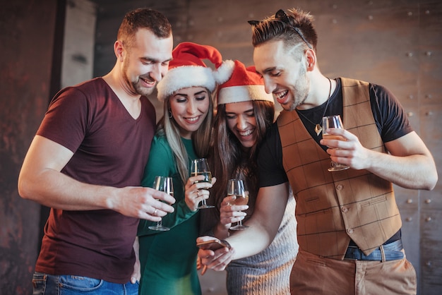 Alegres viejos amigos se comunican entre ellos y miran por teléfono, con copas de champán en la fiesta de año nuevo. Concepto de entretenimiento y estilo de vida. Wifi conectado personas