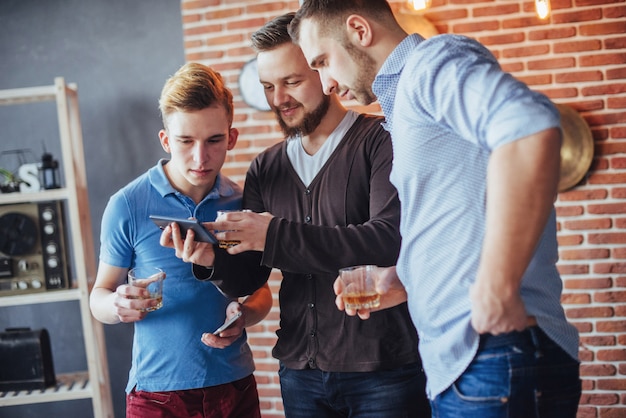 Alegres viejos amigos se comunican entre ellos y miran por teléfono, vasos de whisky en el pub. estilo de vida de entretenimiento Wifi conectado a personas en la mesa de bar