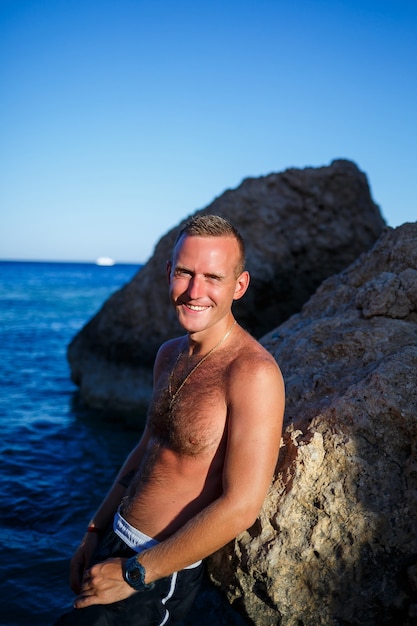 Alegría de chico hombre feliz de vacaciones, se encuentra en la orilla y mira al mar. Pantalones cortos de hombre, sol, playa.