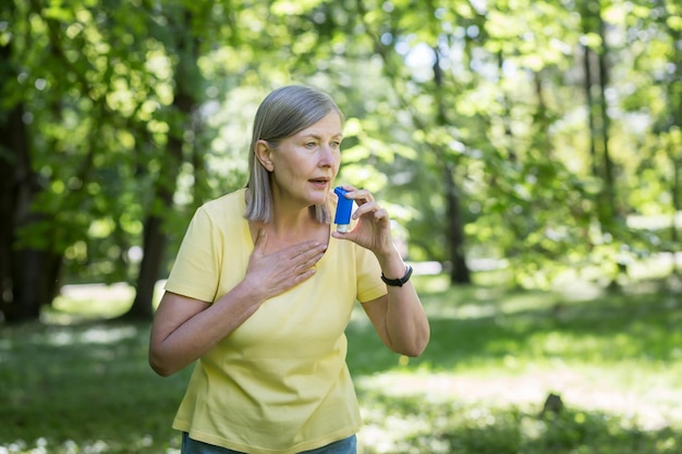 Alergias sazonais Uma mulher mais velha no parque na natureza tem dificuldade em respirar usa um inalador espirra e tosse em um lenço Tem alergia sufoca