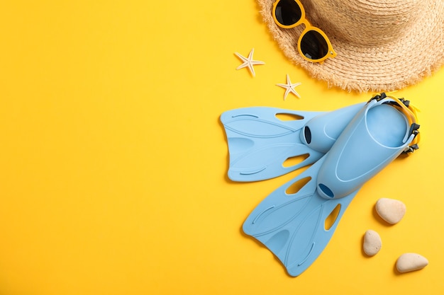 Aletas, sombrero de paja, gafas de sol y estrellas de mar sobre fondo amarillo