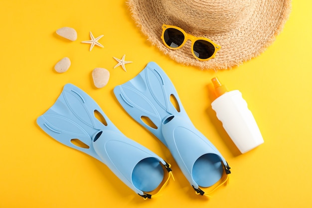 Aletas, sombrero de paja, gafas de sol, protector solar y estrellas de mar sobre fondo amarillo