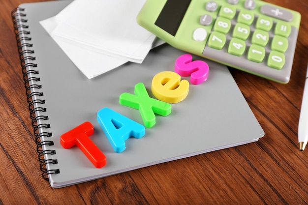 Foto alfabeto taxes y calculadora con cuaderno en mesa de madera