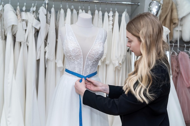 Alfaiate feminino medindo vestido de noiva elegante em manequim usando fita métrica