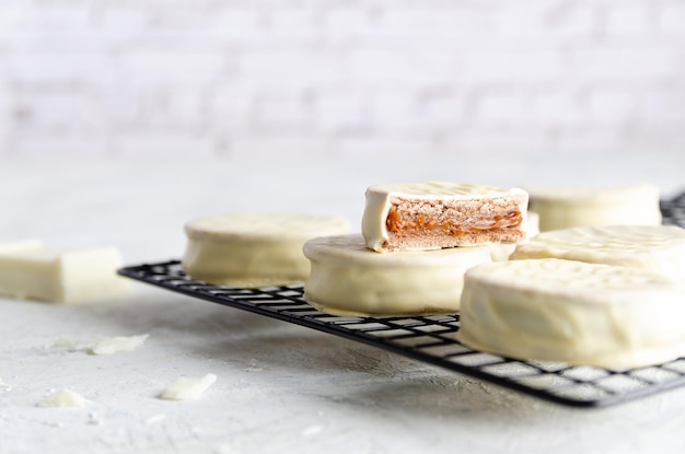 Alfajores aus weißer Schokolade auf einem dunklen Gestell mit einem Stück weißer Schokolade auf hellem Hintergrund.