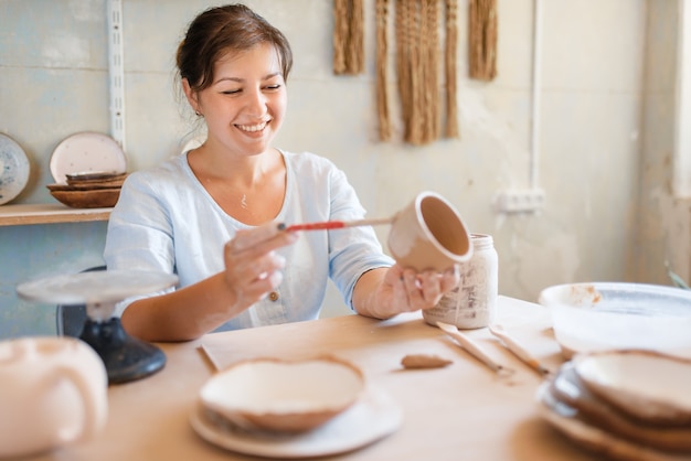 Alfarero femenino pinta una olla, taller de alfarería.