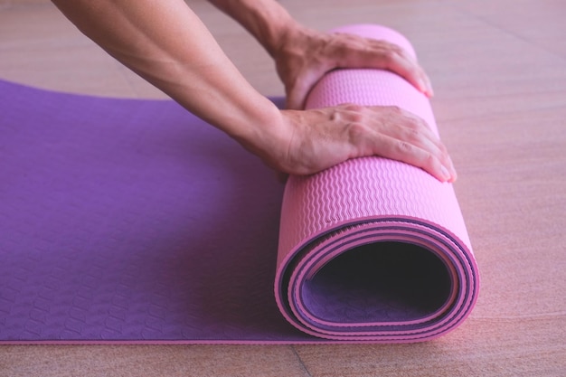 Alfombra de yoga en manos de un hombre en un piso cerca del hombre se extiende alfombra de fitness rosa púrpura