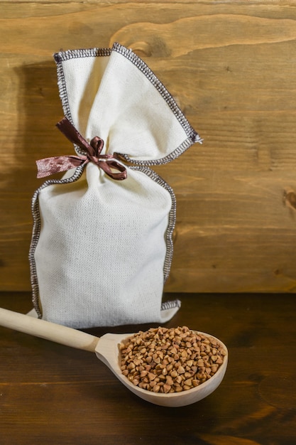 Alforfón en cuchara de madera, junto al saco de lona con grano sobre fondo de madera marrón. Comida sana