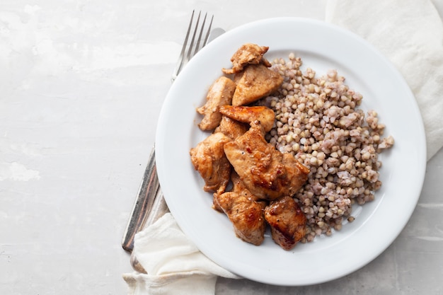 Alforfón hervido con pollo en salsa sobre un plato blanco sobre la mesa de cerámica