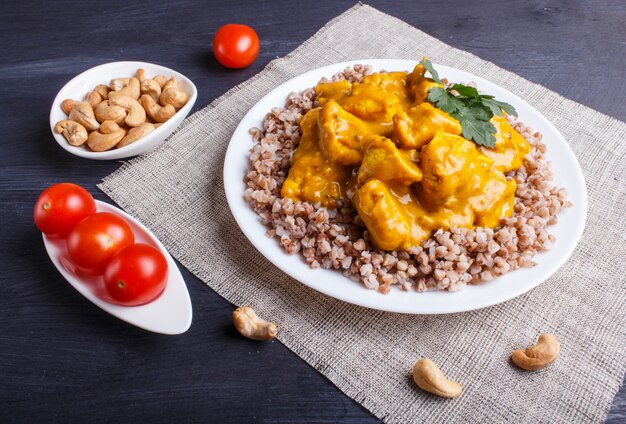 Alforfón con salsa de curry de pollo con anacardo en superficie de madera negra.