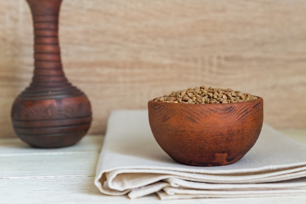 Alforfón seco en un tazón de arcilla marrón en la mesa de madera. grano sin gluten para una dieta saludable