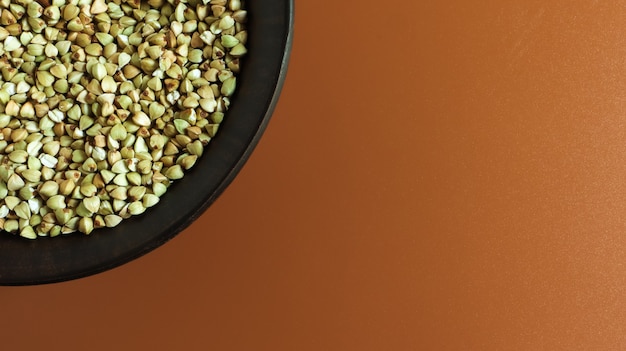 Alforfón verde crudo en una placa de arcilla marrón sobre un fondo marrón. Concepto de comida orgánica vegana.