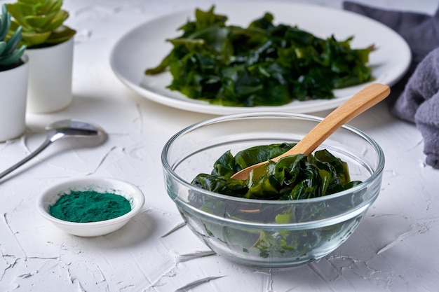 algas laminaria Kelp y polvo de espirulina en un recipiente para vasos con una cuchara de madera de fondo blanco