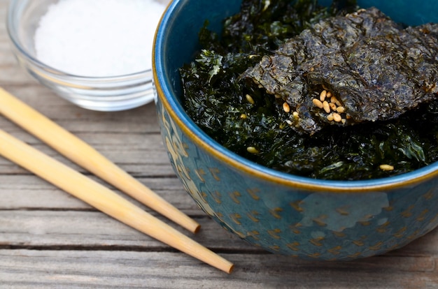 Algas secas tostadas saladas nori con semillas de sésamo en un recipiente azul sobre la vieja mesa de madera