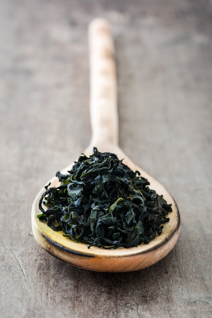 Algas wakame japonesas secas en cuchara de madera sobre mesa de madera