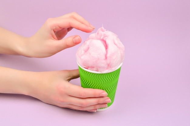 Algodón de caramelo rosa brillante en vaso de plástico en mano de mujer sobre fondo lila