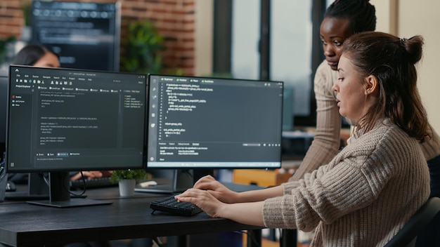 Algoritmo de escrita de programador júnior sob supervisão de colega experiente sentado na mesa com várias telas mostrando a interface de programação. Desenvolvedor escrevendo código com a ajuda do colega.