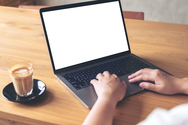 Alguém está usando laptop, com uma xícara de café na mesa de madeira