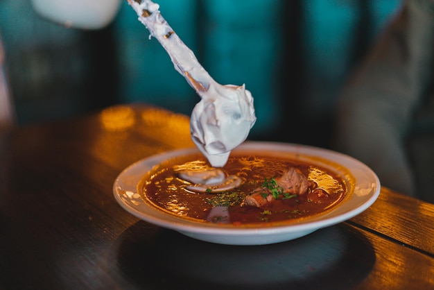 Alguien pone una cucharada de crema agria en un puesto de sopa de remolacha sobre una mesa Cuchara Comida Sopa Tazón Vegetal Pan rústico Cena Crema agria Borshch Tradición Remolacha Sopa de tomate