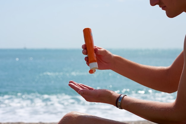 Alguien poniendo crema solar en sus manos en la playa.