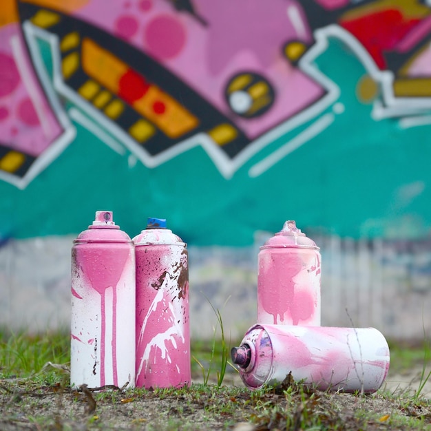 Foto algumas latas de tinta usadas estão no chão perto da parede com uma bela pintura de graffiti em cores rosa e verde conceito de arte de rua