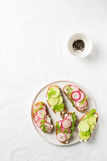 Algumas torradas de rabanete e pepino com ricota e salada com papel e sal