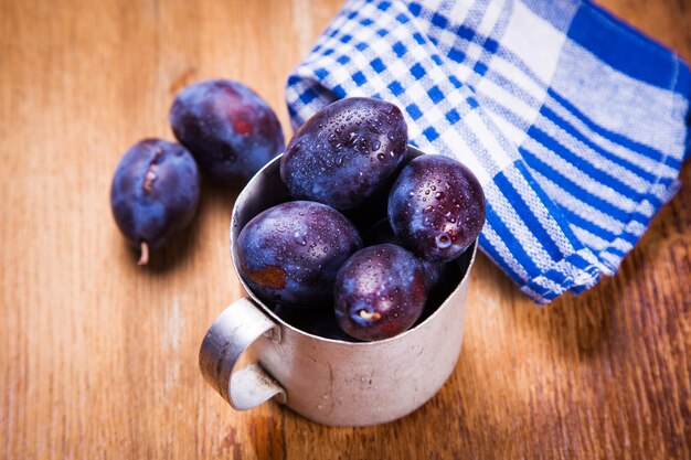 Algunas ciruelas maduras crudas azules en taza vieja en estudio