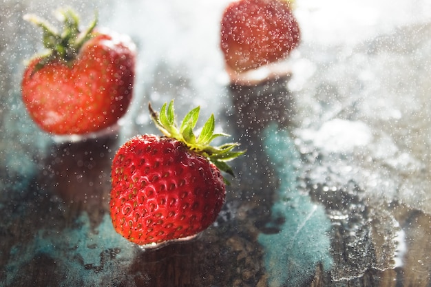 Algunas fresas maduras frescas cultivadas en casa en la superficie de cristal azul claro con gotas de agua de pulverización congelada