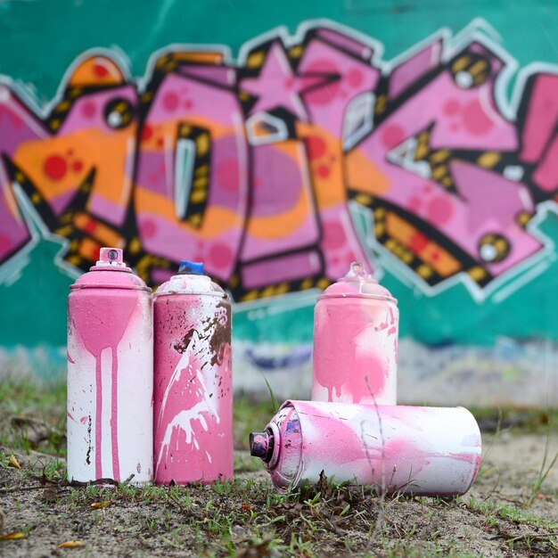 Foto algunas latas de pintura usadas yacen en el suelo cerca de la pared con una hermosa pintura de graffiti en colores rosa y verde concepto de arte callejero