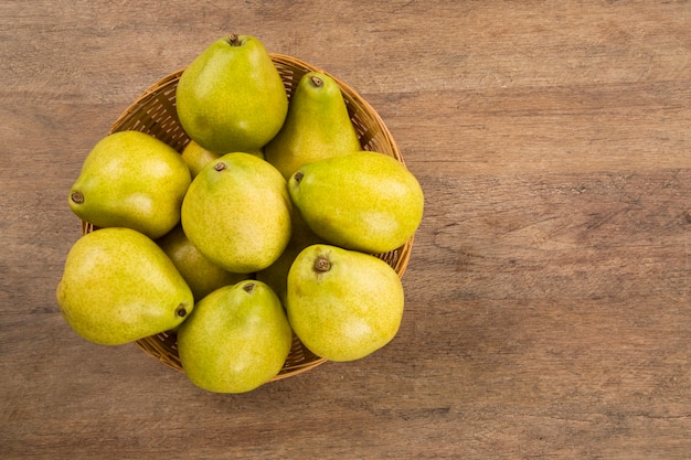 Algunas peras en una canasta sobre una superficie de madera. Frutas frescas