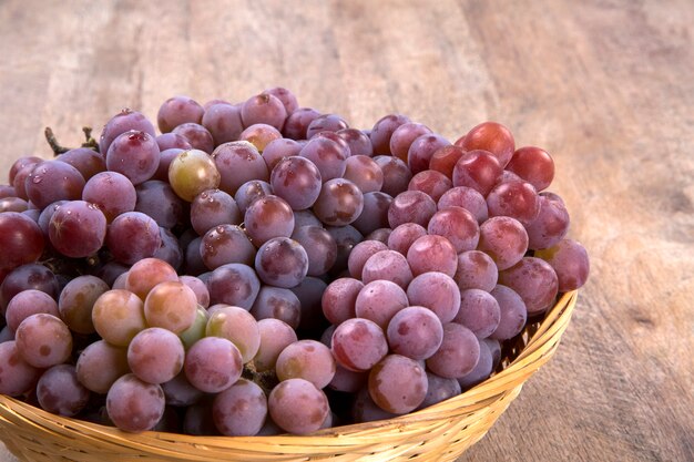 Algunas uvas rojas en una olla de madera sobre una superficie de madera visto desde arriba