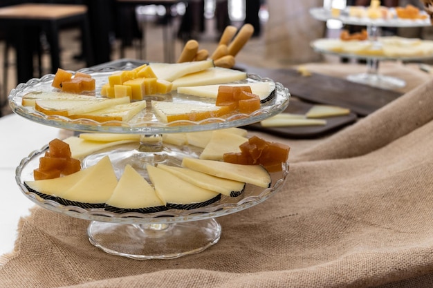 Alguns cubos fatiados de marmelo e queijo em uma mesa com pão e ao fundo pessoas desfocadas